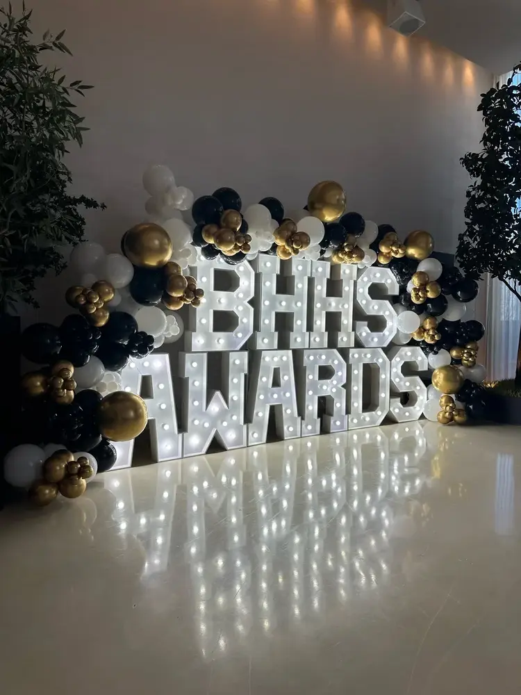 Black, white and gold balloons surrounding illuminated BHHS AWARDS letters. corporate balloon decor design inspiration for Elmhurst; photographed location unverified.