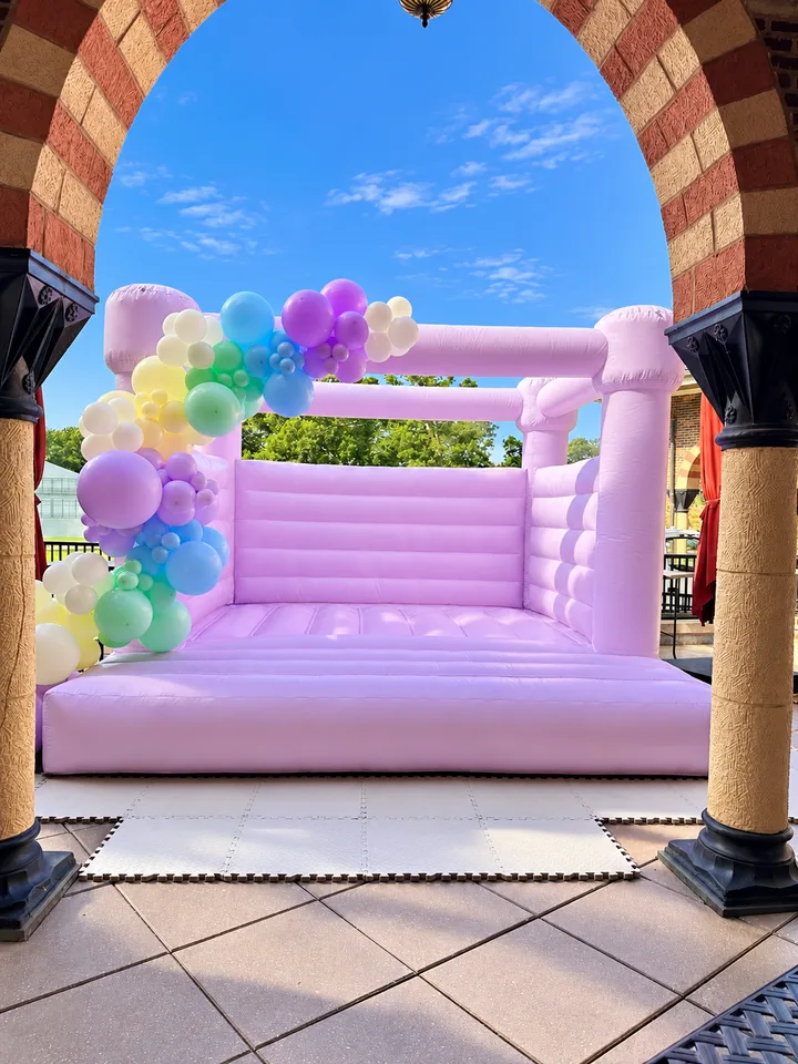 Pastel flower balloons and a garland framing a lavender outdoor bounce house