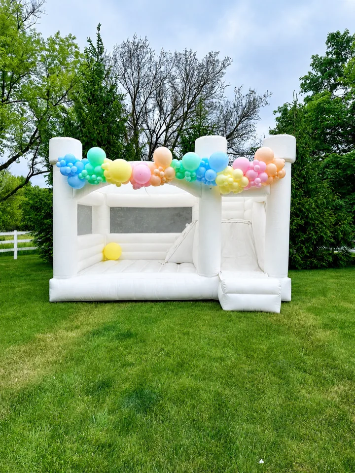 Pastel rainbow balloon garland across the top of a white outdoor bounce house