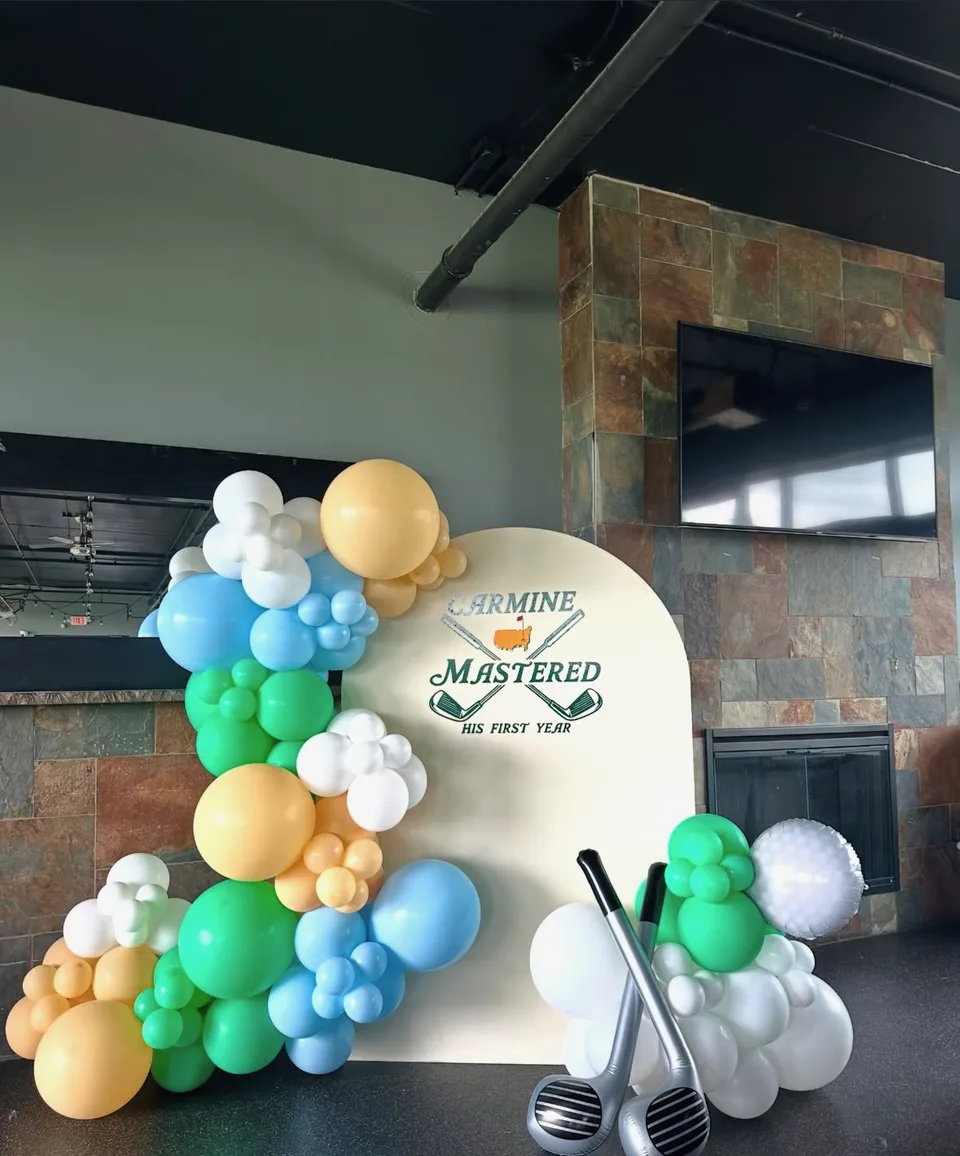 Blue, green, yellow and white balloon clusters around a golf-themed first-birthday backdrop
