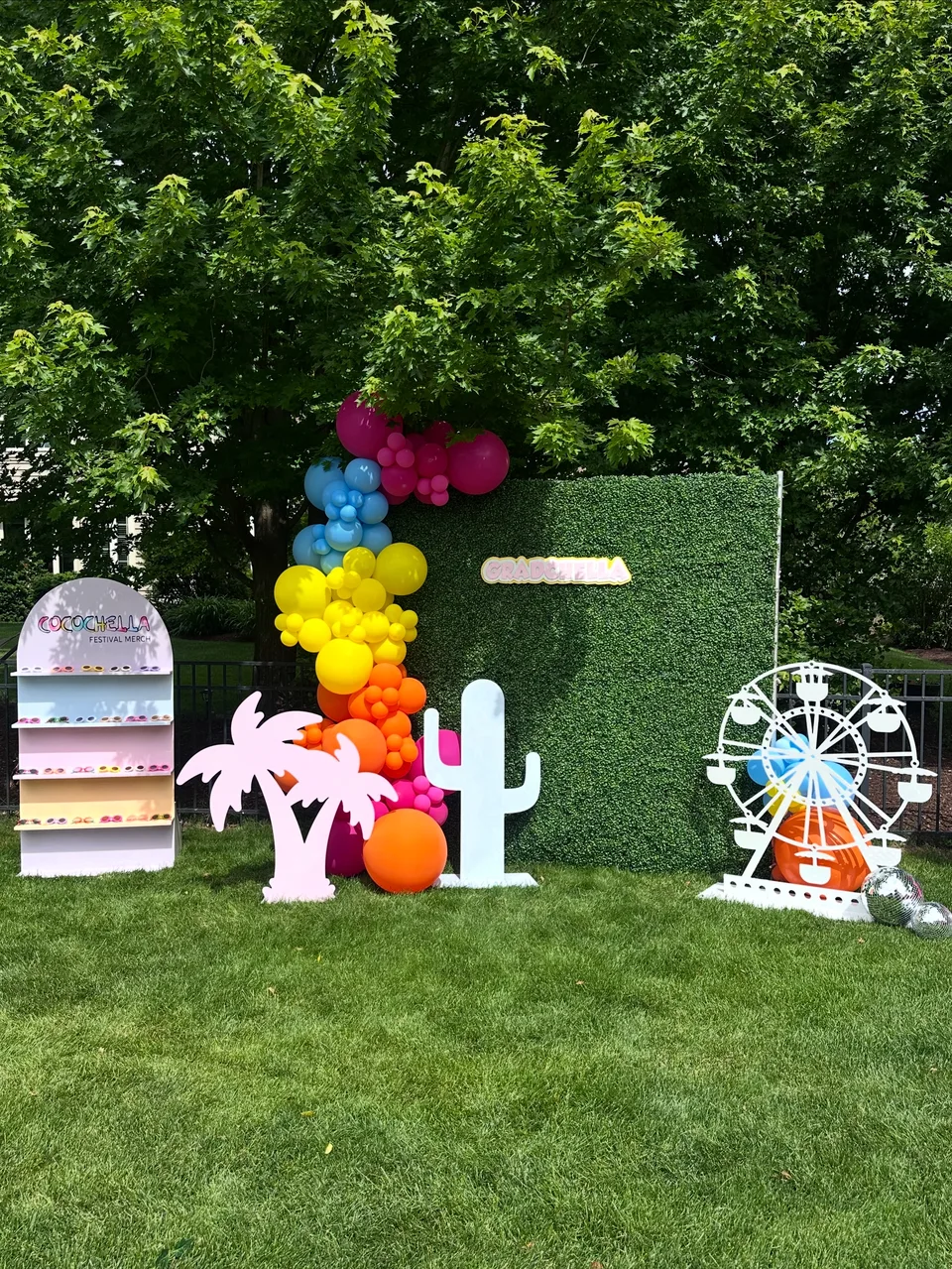 Rainbow balloons beside an outdoor hedge wall with festival-inspired props