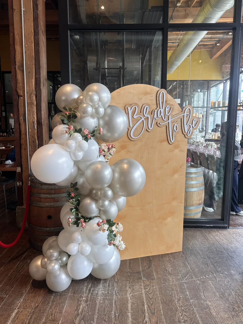 White and silver balloons with small flowers beside a wooden Bride to Be backdrop
