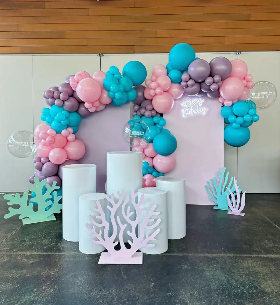 Teal, pink and lavender balloons framing two panels, a Happy Birthday sign and white display plinths